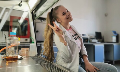 Wyraźnie zadowolona studentka pracująca pod komorą laminarną. 